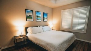 A bedroom with a large bed, two bedside tables with lamps, and three framed pictures on the wall. - Spark Getaways: The Mulligan Spa and Golf (Lubbock)