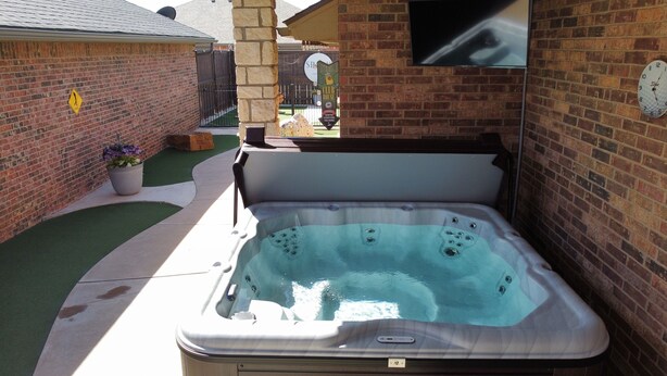 A hot tub in a backyard with a brick wall, a potted plant, and a sign for a club house. - Spark Getaways: The Mulligan Spa and Golf (Lubbock)
