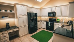 A kitchen with white cabinets, a black refrigerator, a microwave, and a green rug. - Spark Getaways: The Mulligan Spa and Golf (Lubbock)