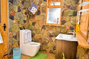 Bathroom features a stone wall, white sink, toilet, and wooden cabinet.