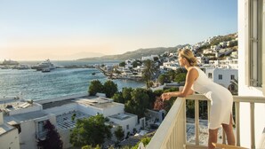 A coastal town with white buildings, a marina with boats, and a person on a balcony overlooking the sea. - Pietra Bianca 1891 Suites Mykonos (Mykonos)