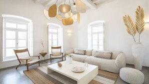 A spacious living room with a large white sofa, two wooden chairs, a coffee table, and a hanging light fixture. - Pietra Bianca 1891 Suites Mykonos (Mykonos)