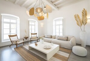 Un ampio soggiorno con un grande divano bianco, due poltrone in legno, un tavolino da caffè e una lampada a sospensione.