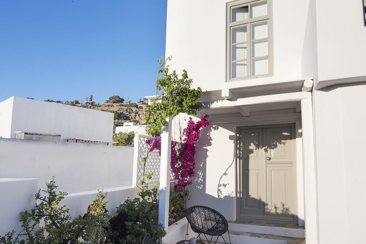 A white building with a stone patio, two black chairs, and a purple flowering plant.