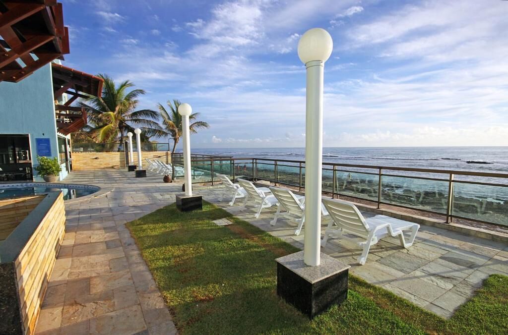 A poolside area with lounge chairs, a pool, and a view of the ocean.