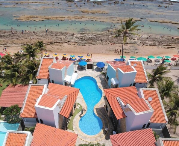 Resort com piscina central rodeada por várias acomodações tipo bangalô, com telhados em tijolos vermelhos.