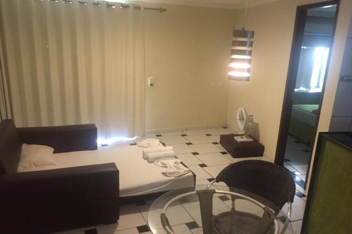 A hotel room with a bed, a sofa, a glass table, a chair, a fan, and a mirror.
