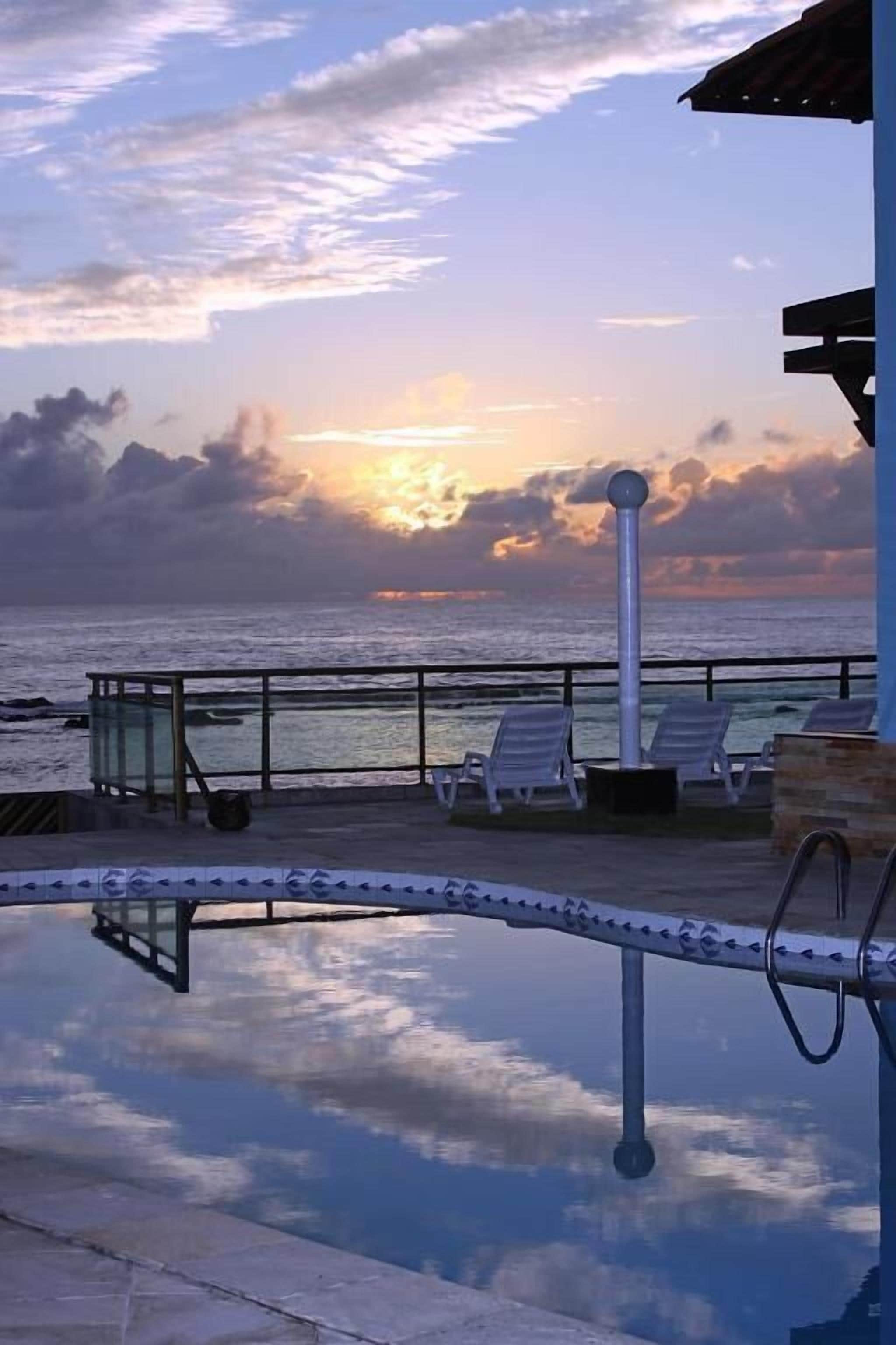 A poolside area with lounge chairs and a view of the ocean at sunset.