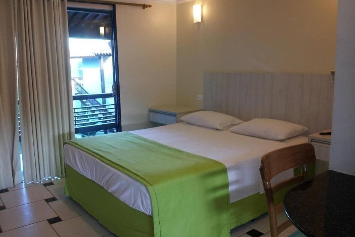 A hotel room with a bed, a chair, a table, a nightstand, and a window with curtains.