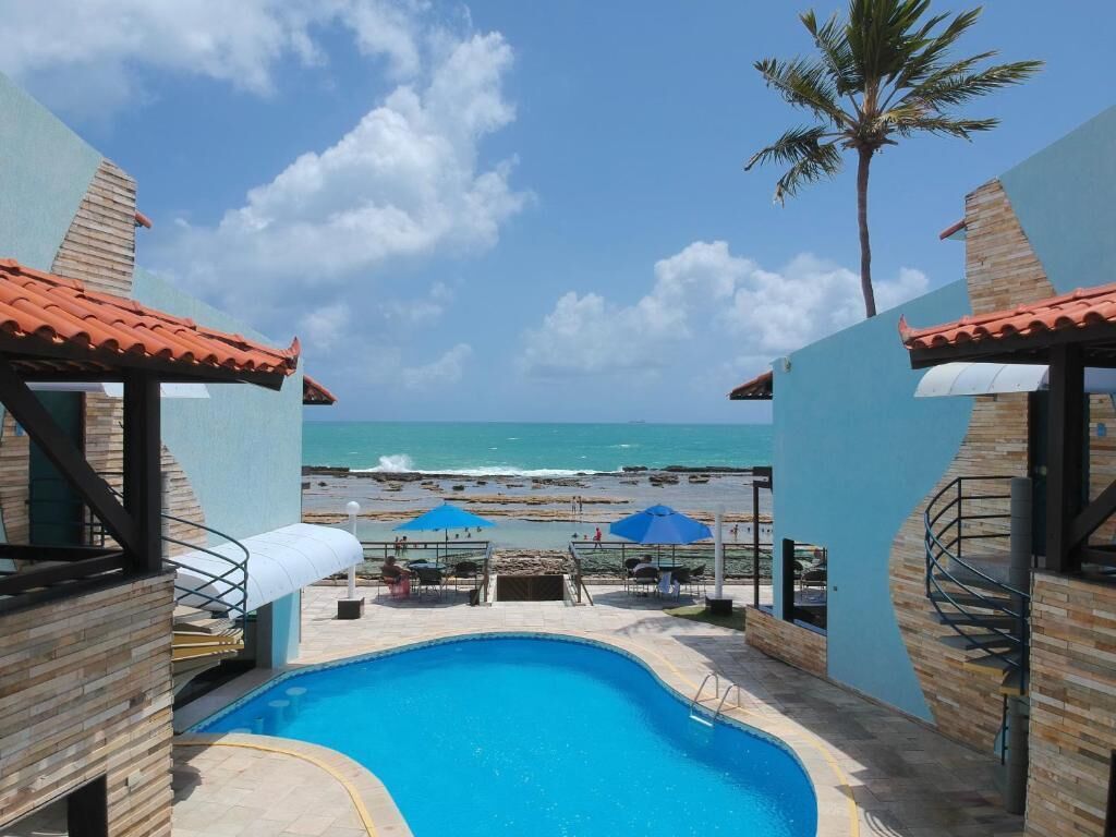 Ein Poolbereich mit Blick auf Strand und Meer, umgeben von Gebäuden mit Ziegeldächern.