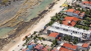 An aerial view of a coastal area with a beach, rocky shoreline, and a cluster of buildings with red-tiled roofs. - Hotel Arrecife dos Corais (Cabo de Santo Agostinho)