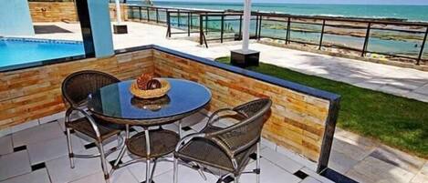 A patio with a round table and wicker chairs, overlooking a pool and beach.