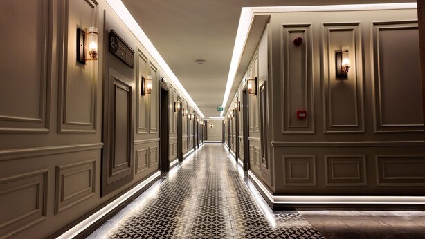 Un pasillo de hotel con piso estampado, relojes en la pared y luminarias.