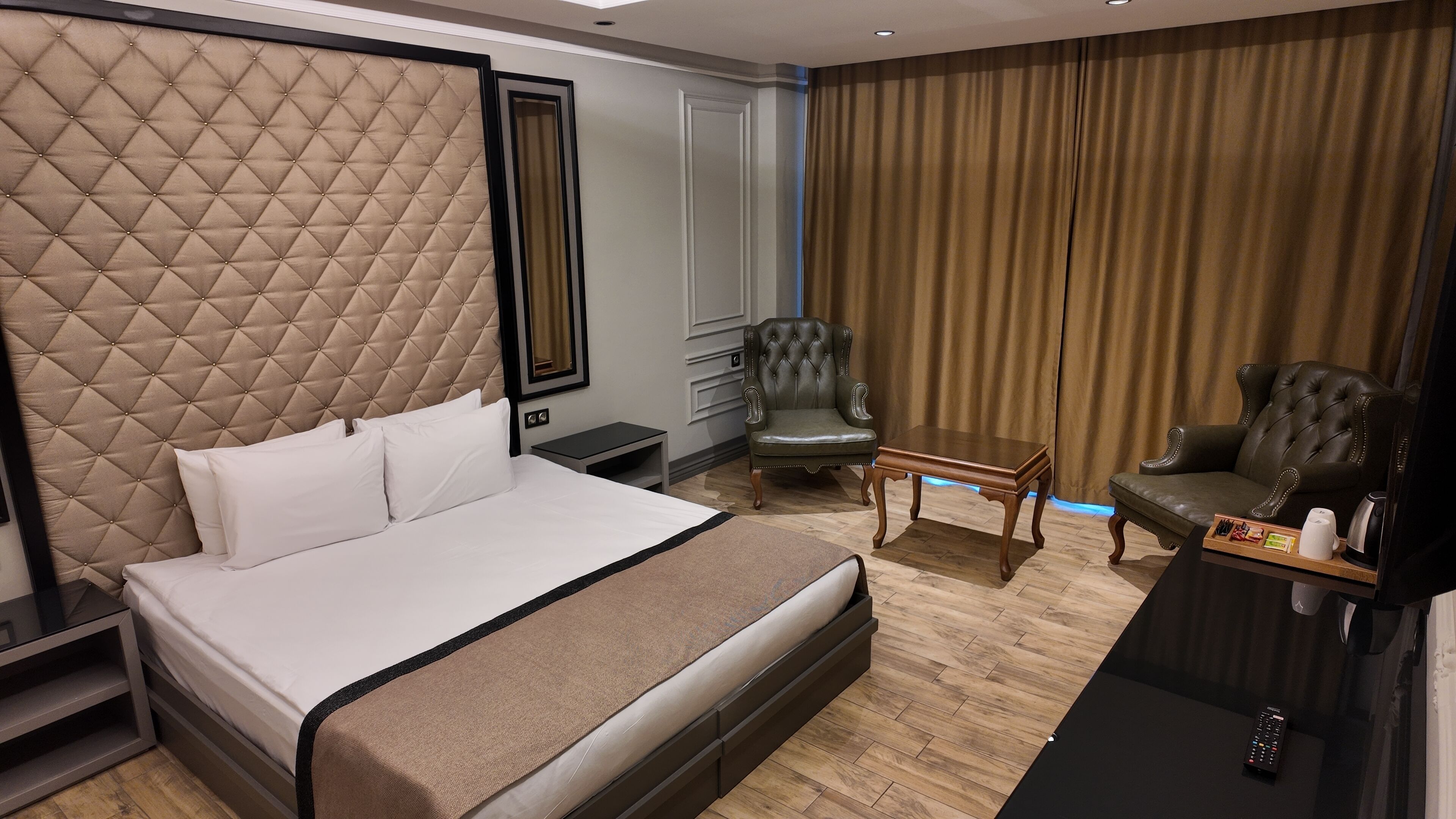 A hotel room with a large bed, two armchairs, a small table, and a TV.