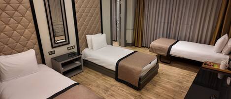 A hotel room with two single beds, a small desk with a chair, a mirror, and a window with curtains.