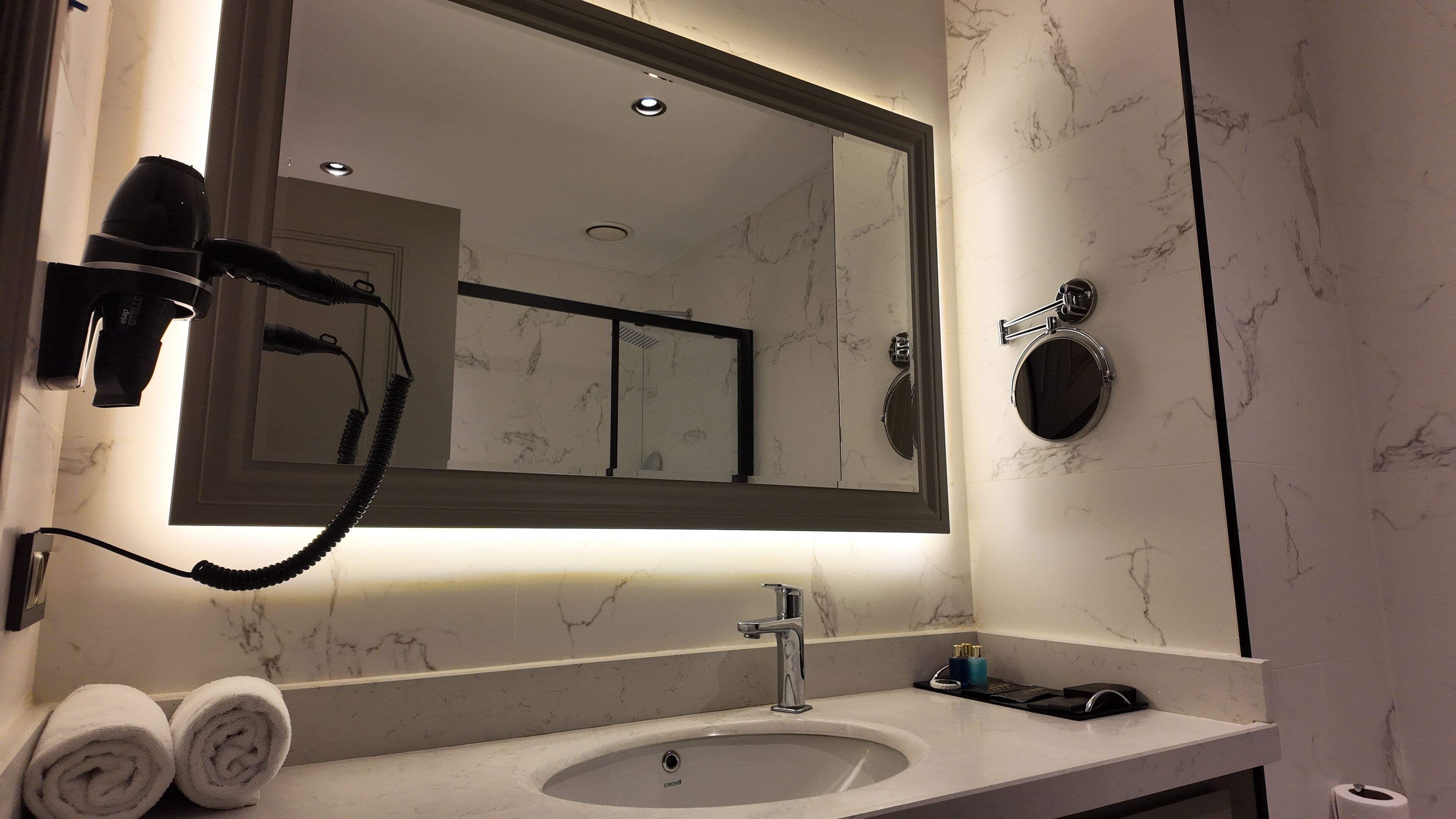 Un baño con lavamanos de mármol, secador de pelo, espejo y toallero.