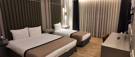 A hotel room with two beds, a desk, a telephone, and a window with curtains.