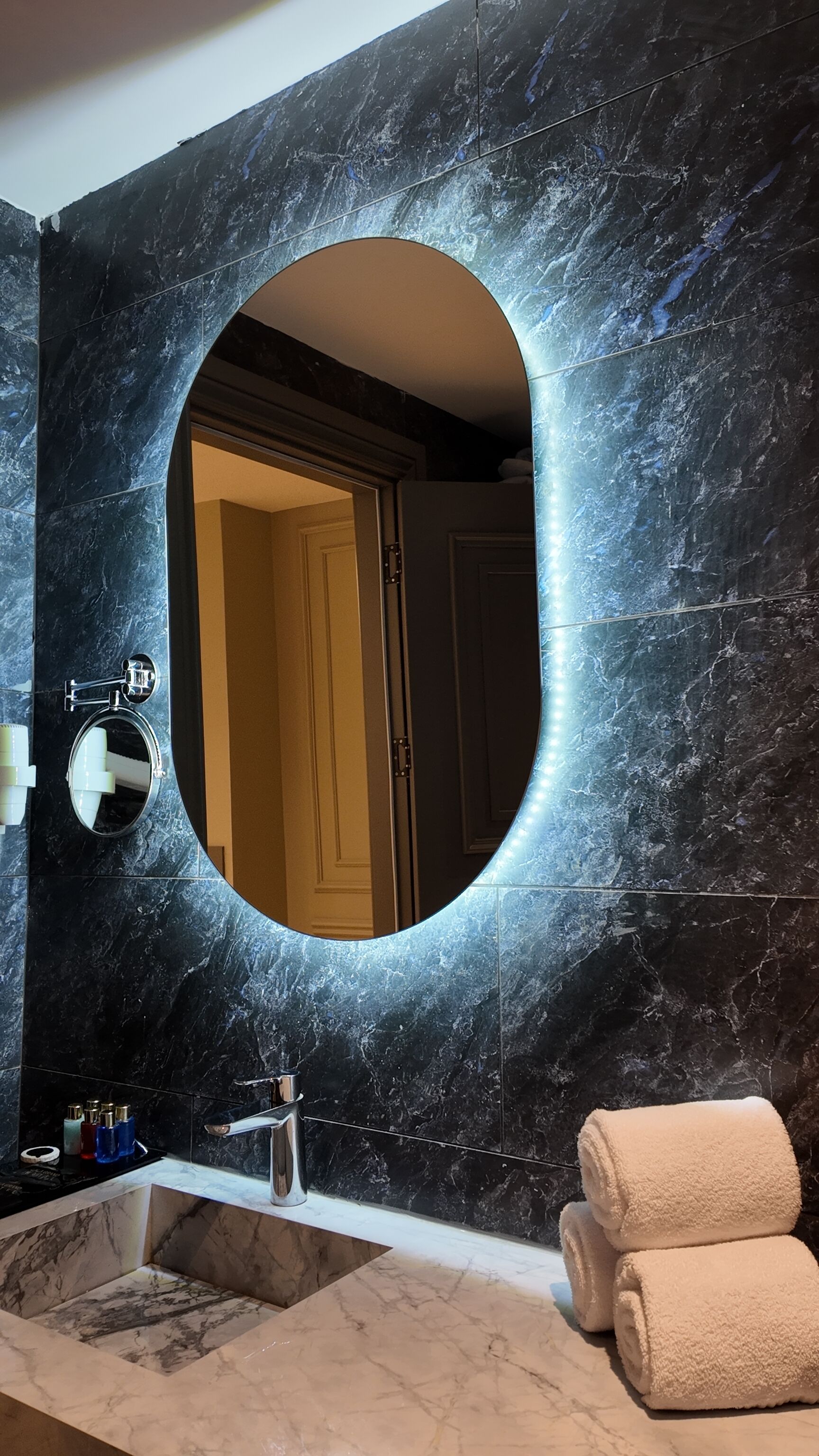 A bathroom with a large mirror, a sink, and a towel rack.