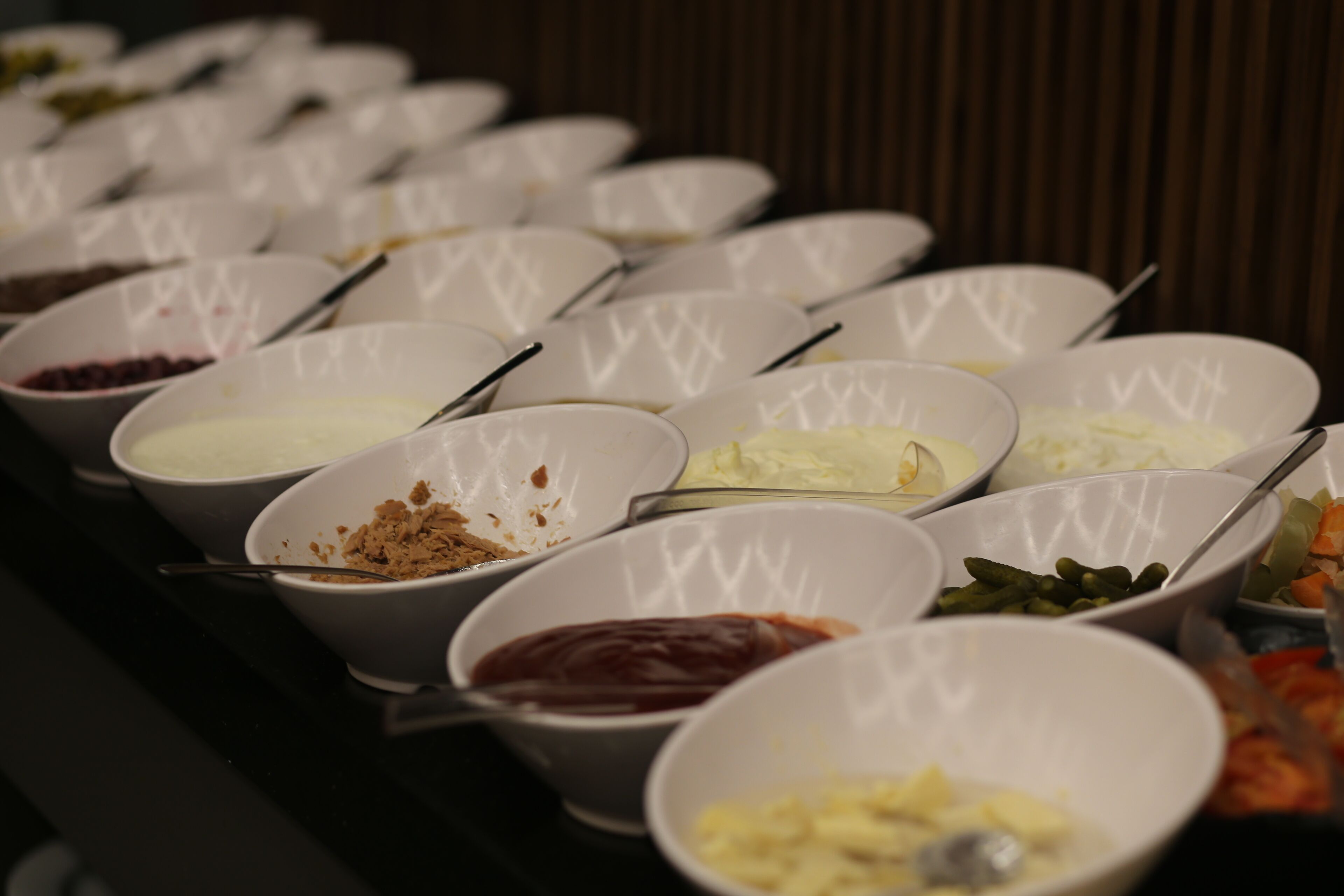 Un buffet con diversi cibi disposti in file, presentati in ciotole bianche.