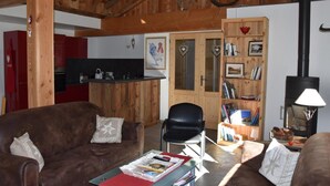 Ein gemütliches Wohnzimmer mit einem braunen Ledersofa, einem schwarzen Sessel und einem kleinen Tisch mit einer Zeitschrift. Im Hintergrund sind ein Bücherregal und ein Kamin zu sehen.