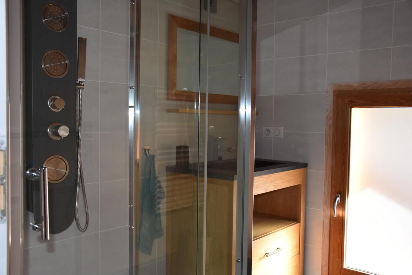 Une douche dotée de plusieurs commandes, d’une porte en verre et d’un meuble en bois sur lequel est accrochée une serviette.