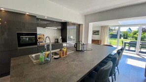 Enjoy meals in the spacious kitchen with a large island, sink, and coffee maker, adjacent to a dining area with a long table and chairs.