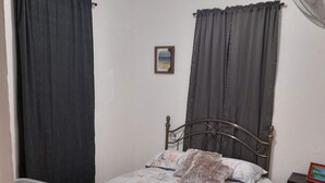 A bedroom with a bed, a bedside table, a fan, and a small picture frame on the wall.