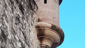A stone tower with a rounded top and a small window, attached to a larger stone wall.