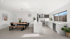 Une cuisine moderne dotée d’un îlot central, d’un coin repas avec une table en bois et d’une grande fenêtre offrant une vue dégagée.