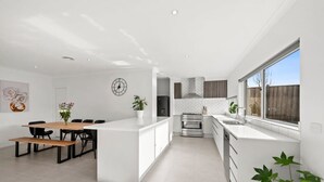 Une cuisine moderne avec des meubles blancs, un îlot central et un coin repas comprenant une table et des chaises en bois.