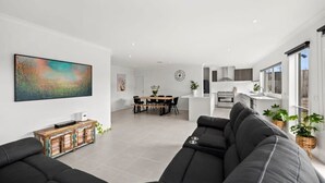 Un salon moderne avec un canapé noir, un coin repas doté d’une table en bois et une cuisine avec des meubles blancs.
