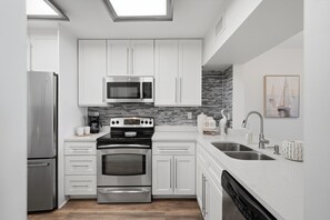 Une cuisine moderne avec des meubles blancs, des appareils en acier inoxydable, un pare-feu en carrelage et une grande fenêtre au-dessus de l’évier.