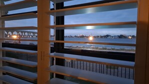 Une vue à travers les persiennes d’une fenêtre, montrant un pont et une vue sur la ville au crépuscule.