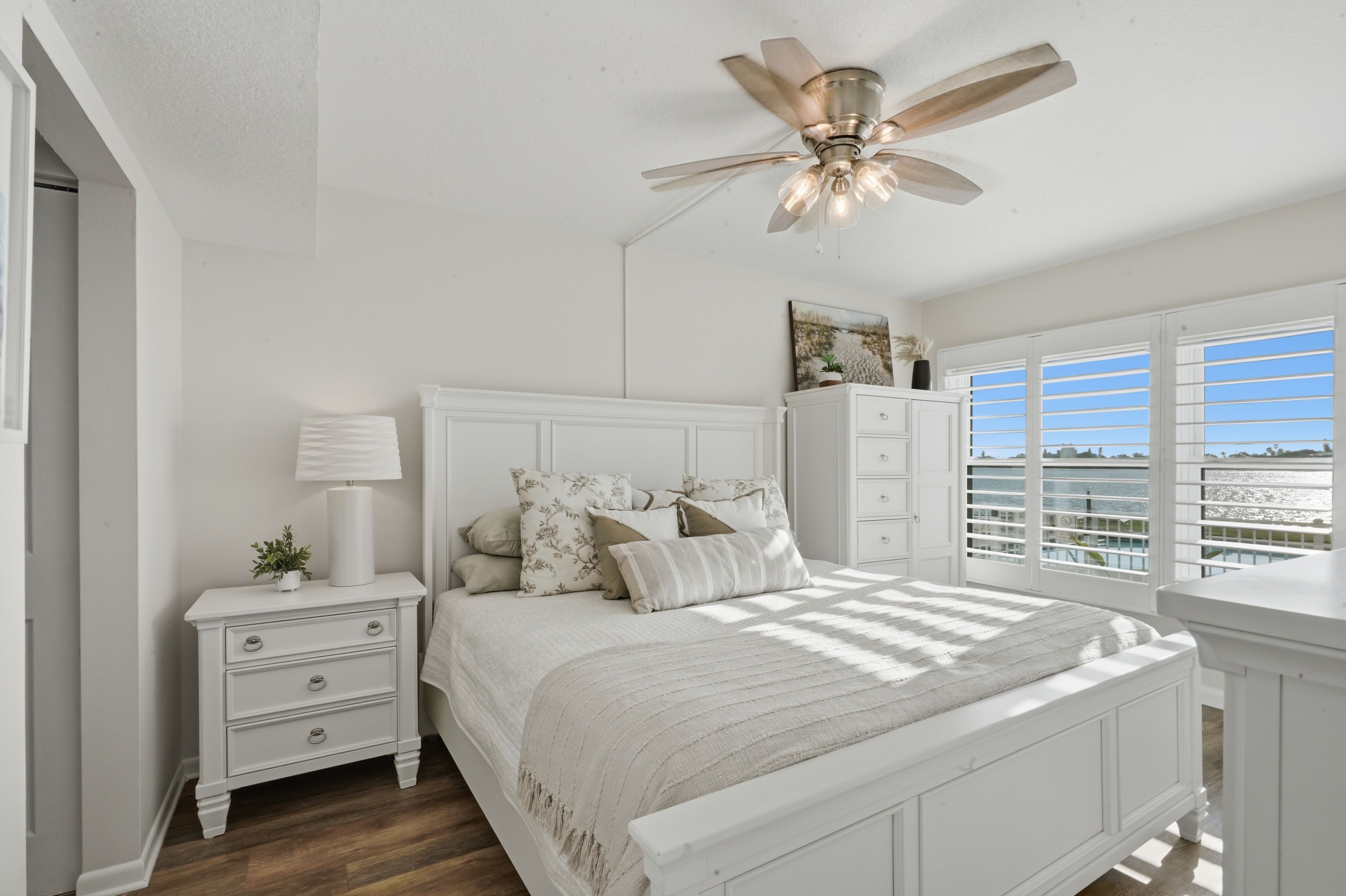 Une chambre à coucher comprenant un lit, des tables de chevet, un ventilateur de plafond, une commode et une fenêtre donnant sur un beau paysage.