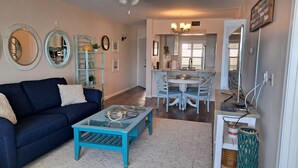 Un salon avec un canapé bleu, une table basse en verre et un coin repas comprenant une table blanche et des chaises bleues.