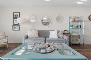 Un salon avec un canapé gris, une table basse en verre surmontée d’un panier en osier, et une bibliothèque en bois bleu clair.