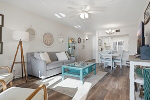 Un salon moderne avec un canapé gris, une table basse et un coin repas comprenant une table et des chaises blanches.