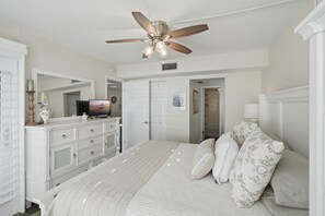 A bedroom with a bed, a dresser, a television, and a ceiling fan.