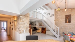 Uma sala de estar ampla com uma mesa de jantar de madeira, uma escada com corrimão branco e uma parede de pedra.
