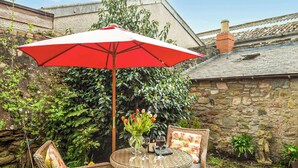 A wicker table with chairs and a red umbrella in a garden setting. - 1 bedroom accommodation in Kelso (Kelso)