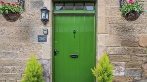 A green door with a 'Welcome' mat, two potted plants, a lantern, and a sign reading 'Hideaway cottage The Butts'. - 1 bedroom accommodation in Kelso (Kelso)