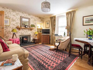 A cozy living room with a fireplace, a sofa, a television, and a dining area with a table and chairs. - 1 bedroom accommodation in Kelso (Kelso)