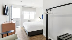 Ein Hotelzimmer mit Bett, Schreibtisch, Stuhl, Fernseher und Kleiderhaken.