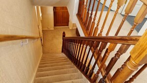 Una escalera con alfombra, balaustres y barandillas de madera, que conduce a un espacio interior con una puerta y piso alfombrado.