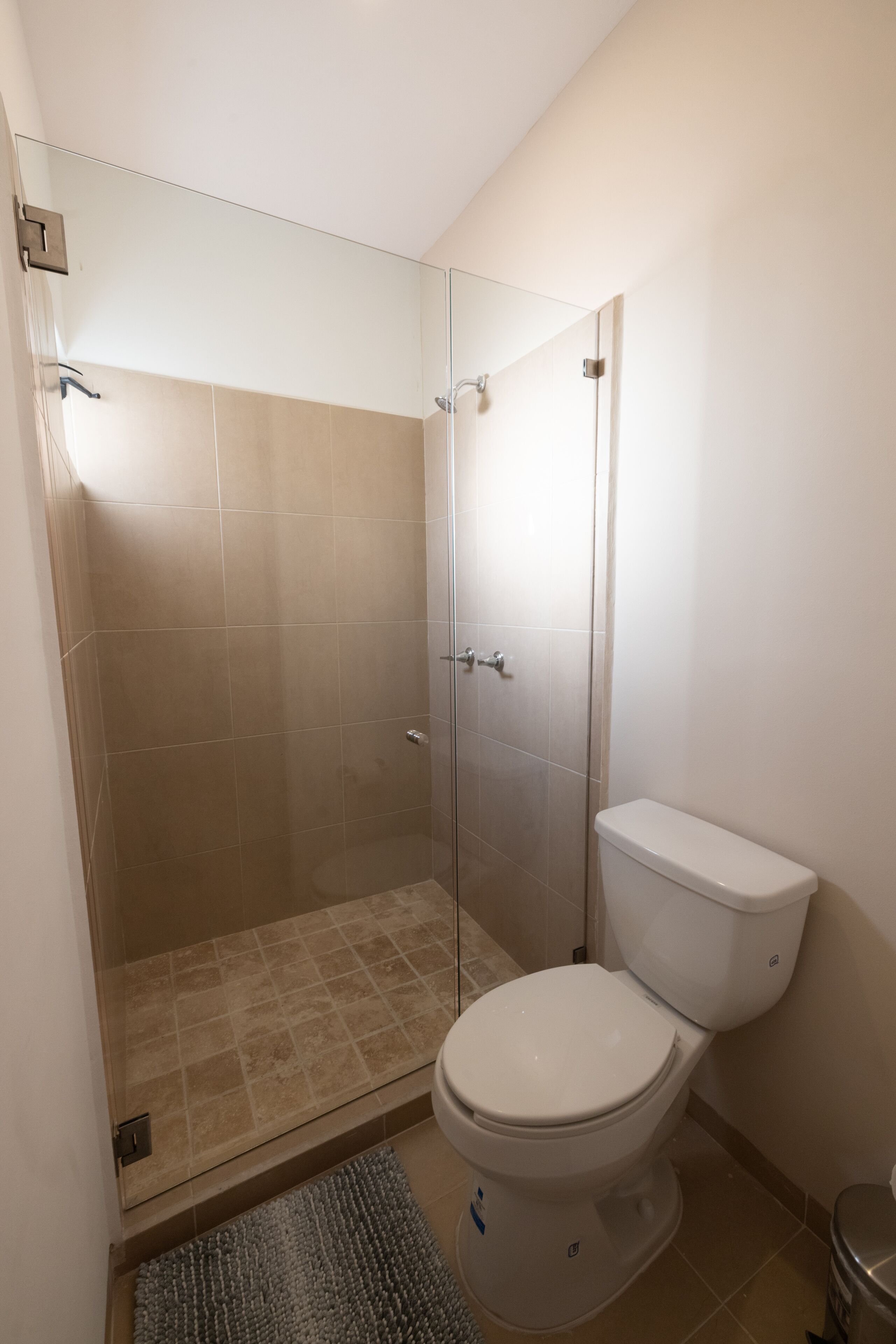 Un bagno con doccia vetrata, un water bianco e pavimento piastrellato.