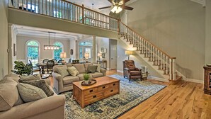 A spacious living room with a high ceiling, a wooden staircase, and a large window. - Lakefront family home w/ private 2-story dock & NEW outdoor deck for dining! (Dawsonville)