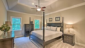 A four-poster bed with a dark finish, a ceiling fan, two windows with views of greenery, and a nightstand with a lamp. - Lakefront family home w/ private 2-story dock & NEW outdoor deck for dining! (Dawsonville)
