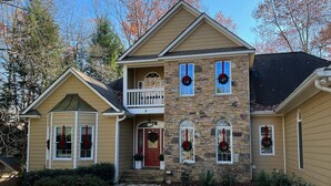A two-story house with a stone facade, a balcony, and a front porch. - Lakefront family home w/ private 2-story dock & NEW outdoor deck for dining! (Dawsonville)