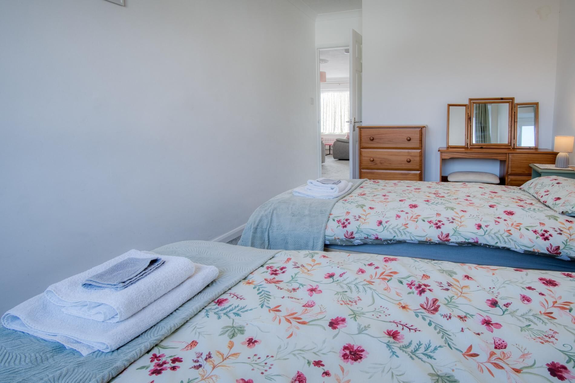 Une chambre avec deux lits, une commode en bois, un miroir et une table de chevet avec une lampe.