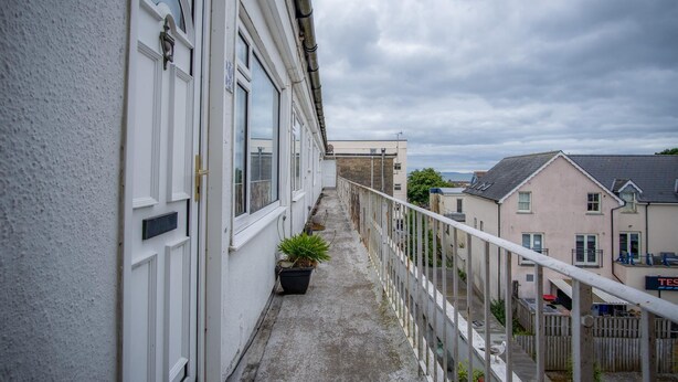 Ein schmaler Balkon mit einem Blumentopf, einem weißen Geländer und Blick auf angrenzende Gebäude.